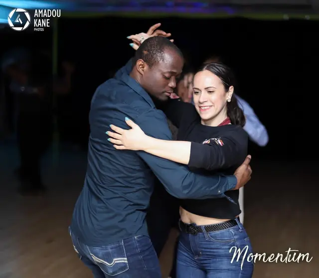 Baggio et une partenaire en position fermée de kizomba sur une piste en bois.